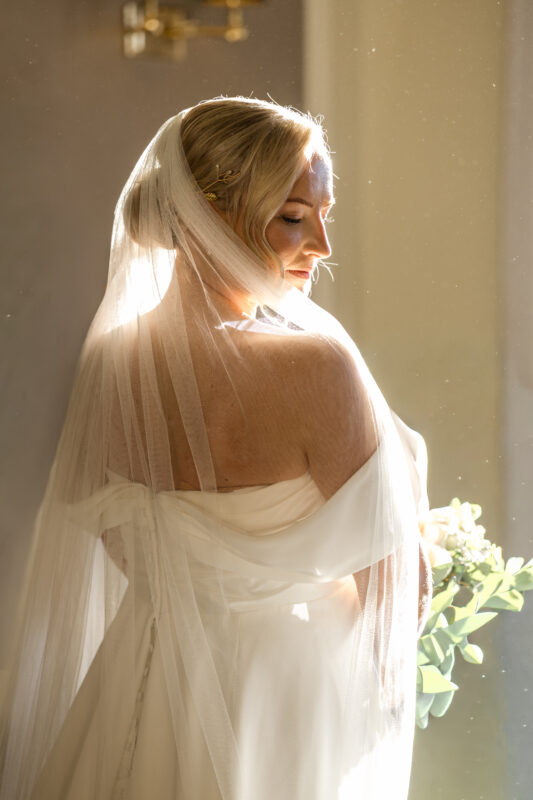 Bride in an off-the-shoulder wedding dress and long veil illuminated by warm natural light at Cornhill Castle.