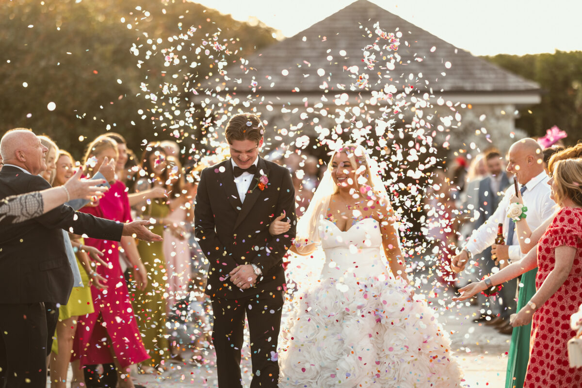 Newlyweds walking through a shower of colourful confetti as wedding guests celebrate outside Radstone Hotel.